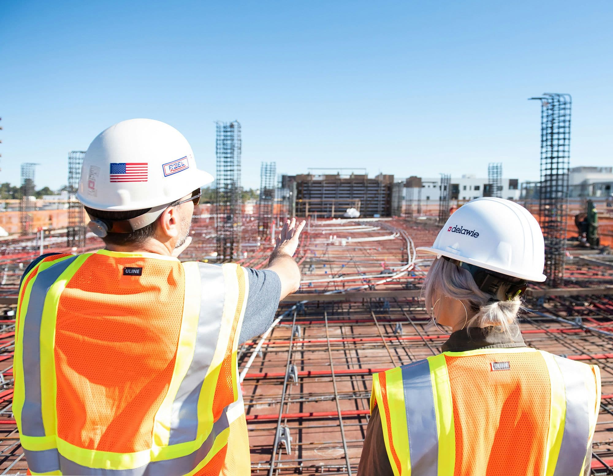 Two site workers in hi-vis and hard hats surveying a construction site